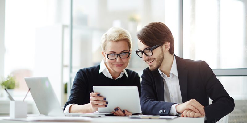 Contemporary employees with digital tablet watching video conference or online seminar while sitting in office